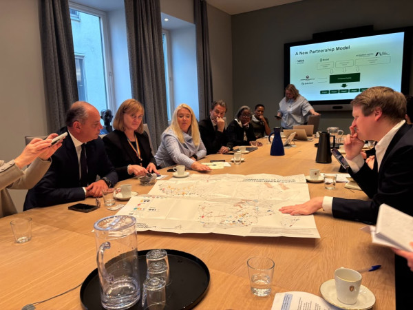 Business meeting in conference room with people seated around table viewing presentation on screen